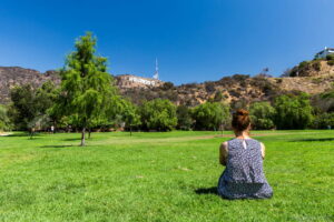 A woman sitting on the grass in a park with a view of Los Angeles.