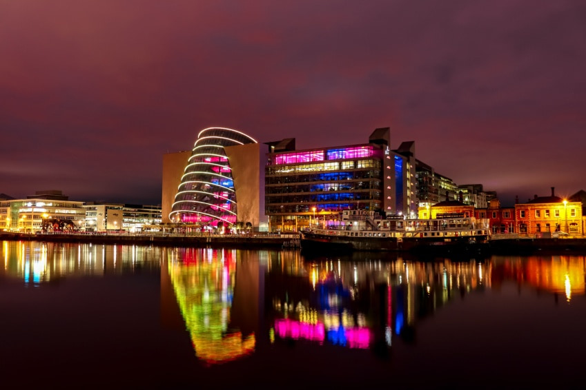 Nighttime view of Dublin city illuminated with reflections shimmering on the River against a dark sky.