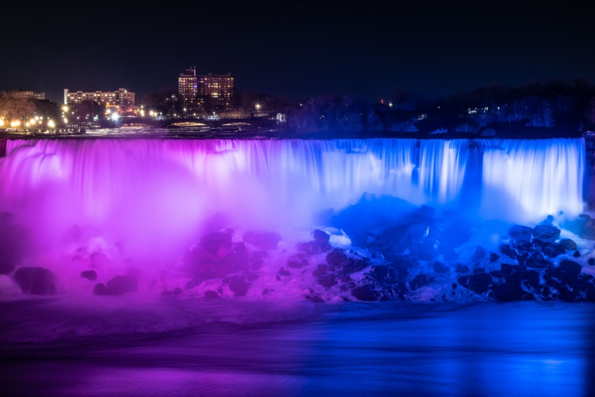 Blurred streams of the American and Bridal Veil falls at Niagara Falls, illuminated in blue and purple in the evening.