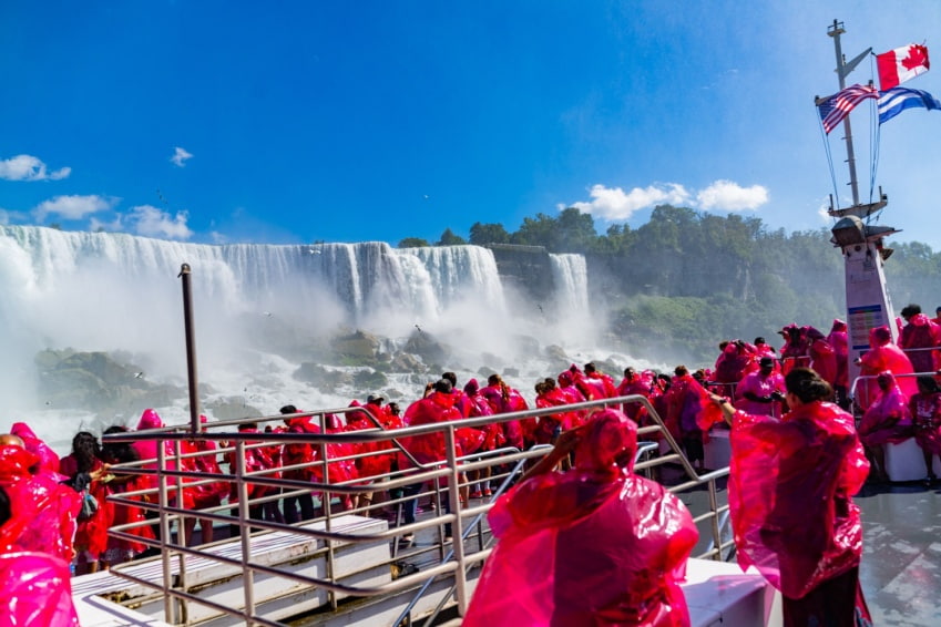 Tourists wearing rain jackets the famous Maid of the Mist boat tour, with the Canadian and American flag flying on the mast of Niagara Cruise.