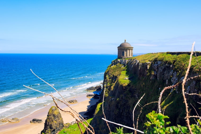 Mussenden Temple perched on Northern Ireland’s North-Western coastline with blue sky and the Atlantic Ocean in the background.