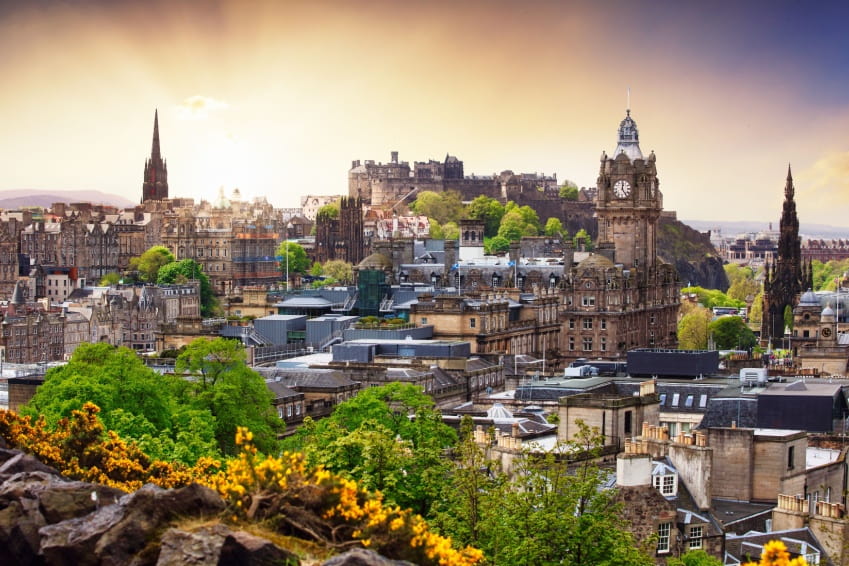 Panoramic view of Edinburgh city skyline with historic castle and clock tower at sunset.