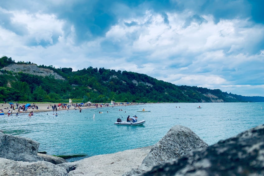 Scenic view of Bluffer’s Park Beach with people on kayaks on turquoise water and dramatic cliffs along the shoreline.